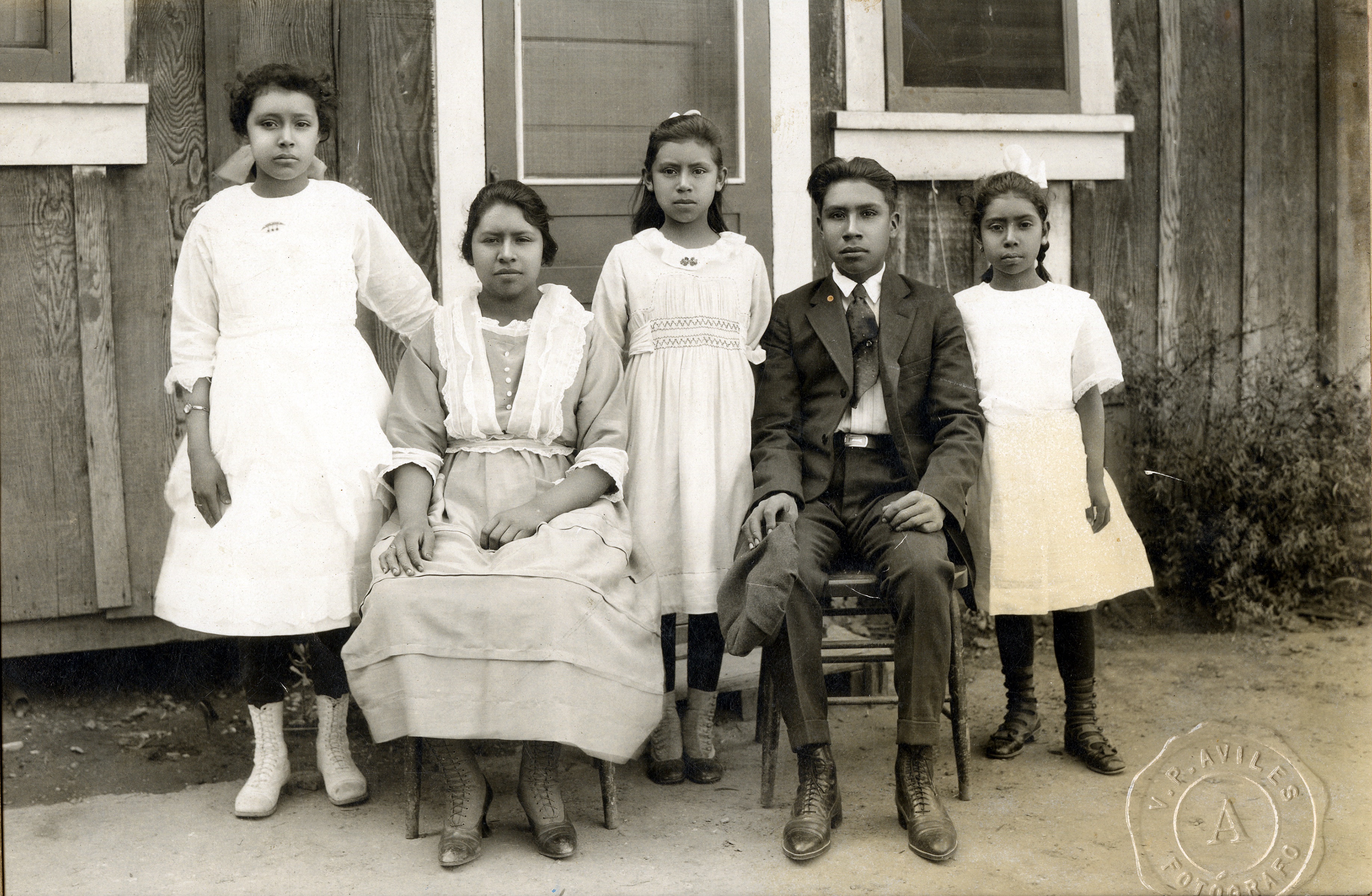 Black and white outdoor photo of three children standing, two young adults seated, posed for portrait.