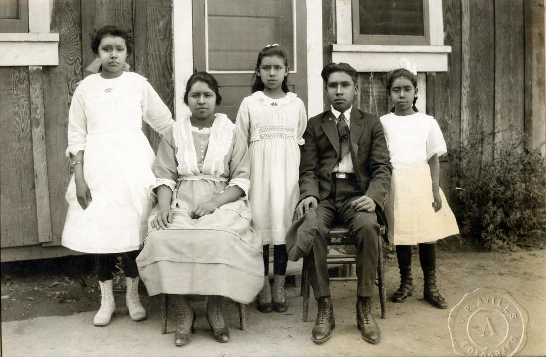Black and white outdoor photo of three children standing, two young adults seated, posed for portrait.