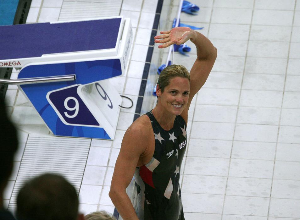 Dara Torres waves to camera next to Olympic swimming pool.  