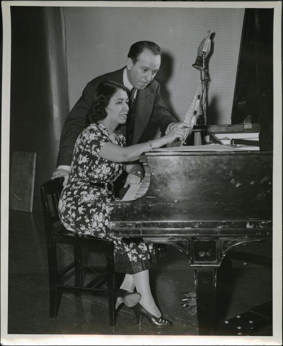 Clotilde Arias sitting at a piano pointing to sheet music with the Argentine composer Terrig Tucci 