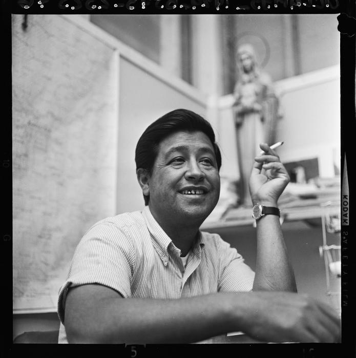 Black and White Photo of Cesar Chavez holding a cigarette and smiling 
