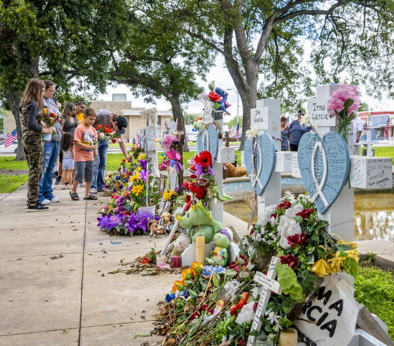 Color photo of twelve people, two cross memorials of Irma Garcia and Joe Garcia, and several other cross memorials.