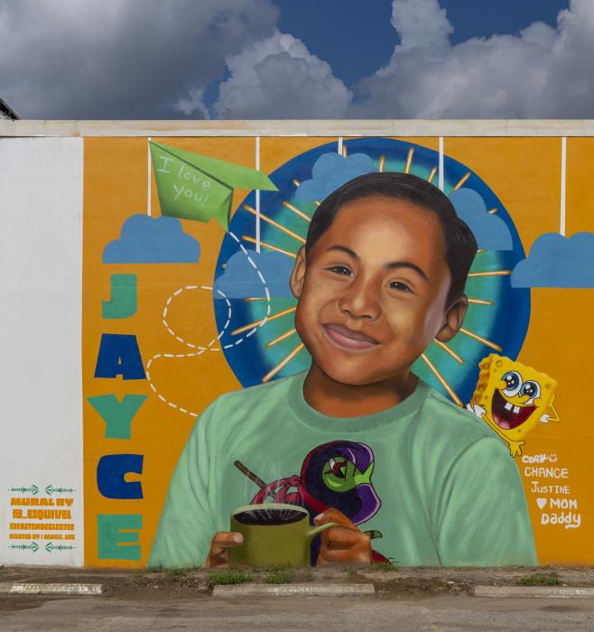 Color photo of portrait mural of Jayce Carmelo Luevanos wearing a teal T-shirt against an orange background. 