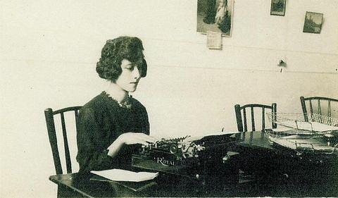 Juana Gallegos sitting a table using a typewriter.  