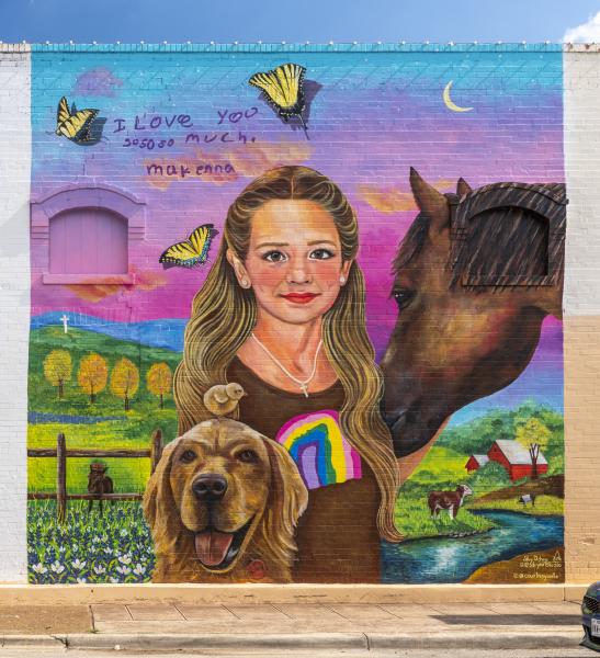 Color photo of portrait mural of Makenna Lee Elrod wearing brown shirt with a rainbow against a colorful rendition of a ranch. 
