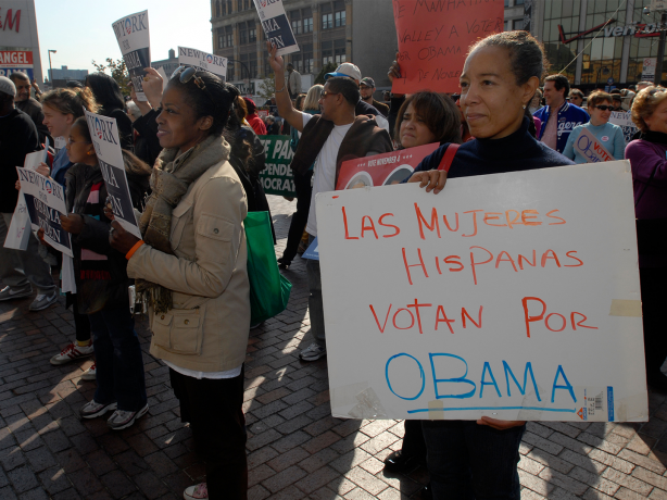 una mujer sostiene un cartel blanco con texto escrito a mano en naranja y azul que dice: “¡Las mujeres hispanas votan por Obama!”.