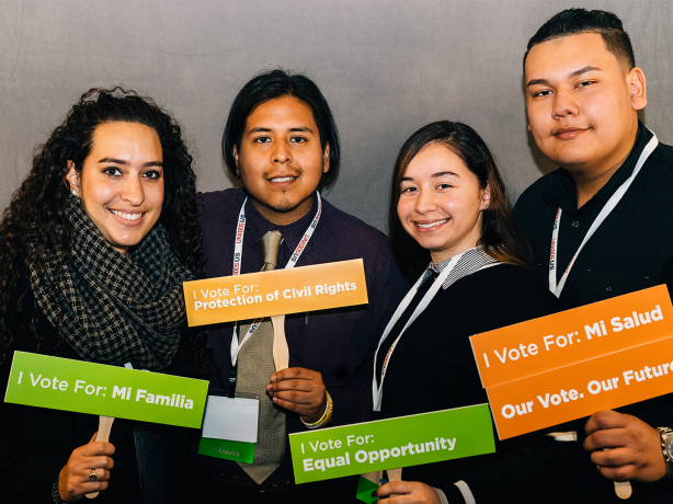 Color photo of four smiling adults holding signs about voting