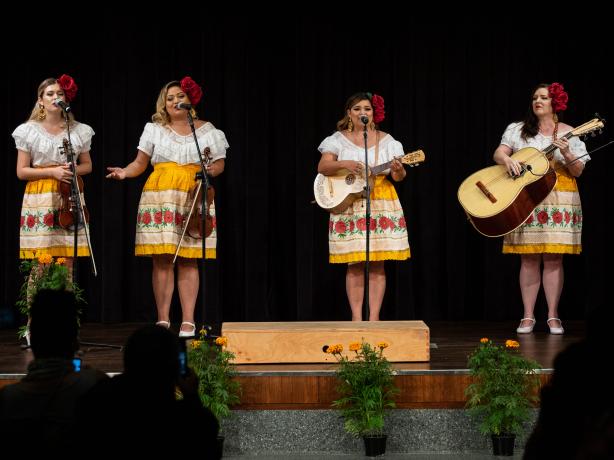 Three women on a stage singing and playing instruments