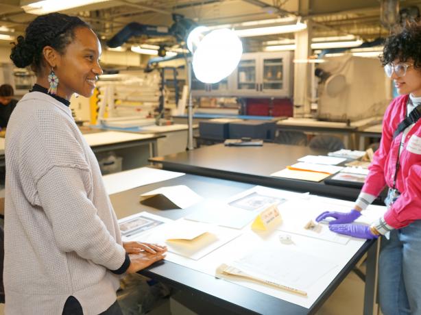 Two interns stand on opposite sides of a table showcasing their museum conservation project.  