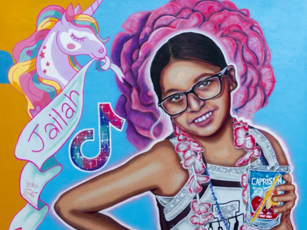 Color photo of portrait mural of Jailah Nicole Silguero wearing a silver cheerleading uniform against a blue and orange background.