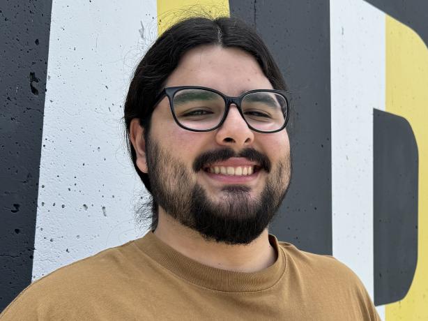 Headshot of a man wearing a brown t-shirt and black glasses.
