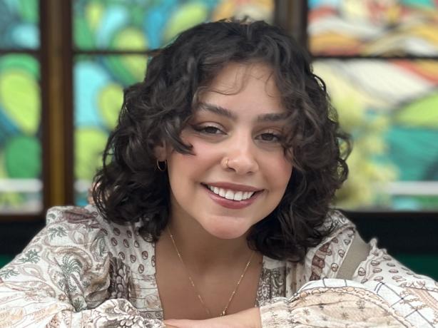 Headshot of a women wearing a patterned cream and brown blouse and gold jewelry.