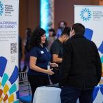 Individuals engaging in a conversation at an event for the National Museum of the American Latino, featuring informational banners with the title "A Cultural Experience: A Profound Journey" and a QR code.
