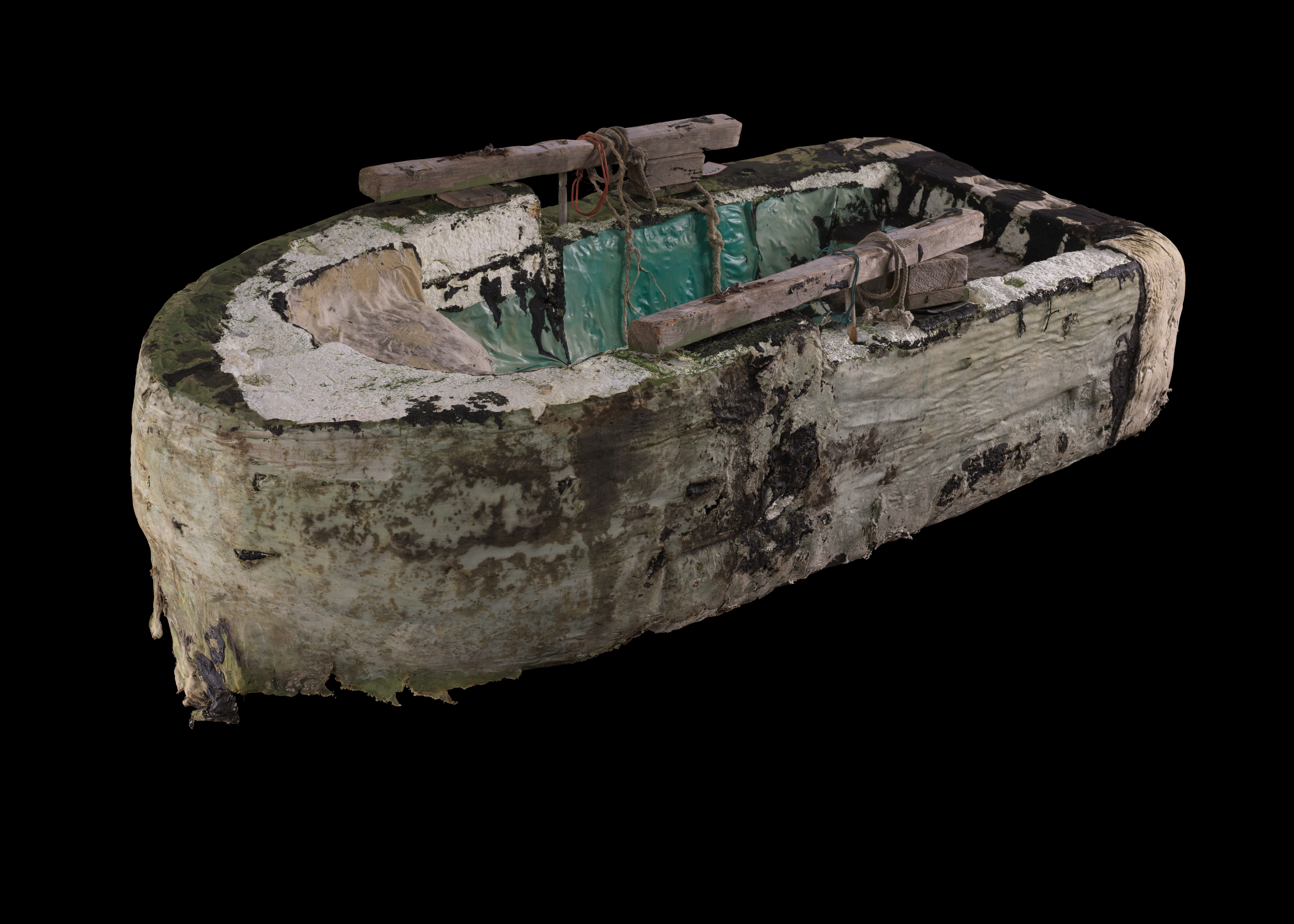 00808-D2-2021.11.03.png Color photo of moldy, worn raft covered in white cloth; two wooden oars wrapped to top with rope