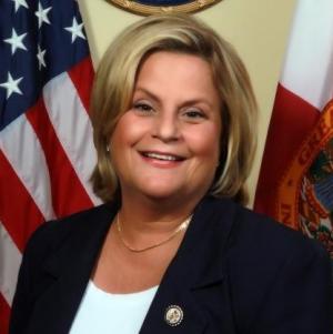 Headshot of Ileana Ros-Lehtinen with two flags in the background.