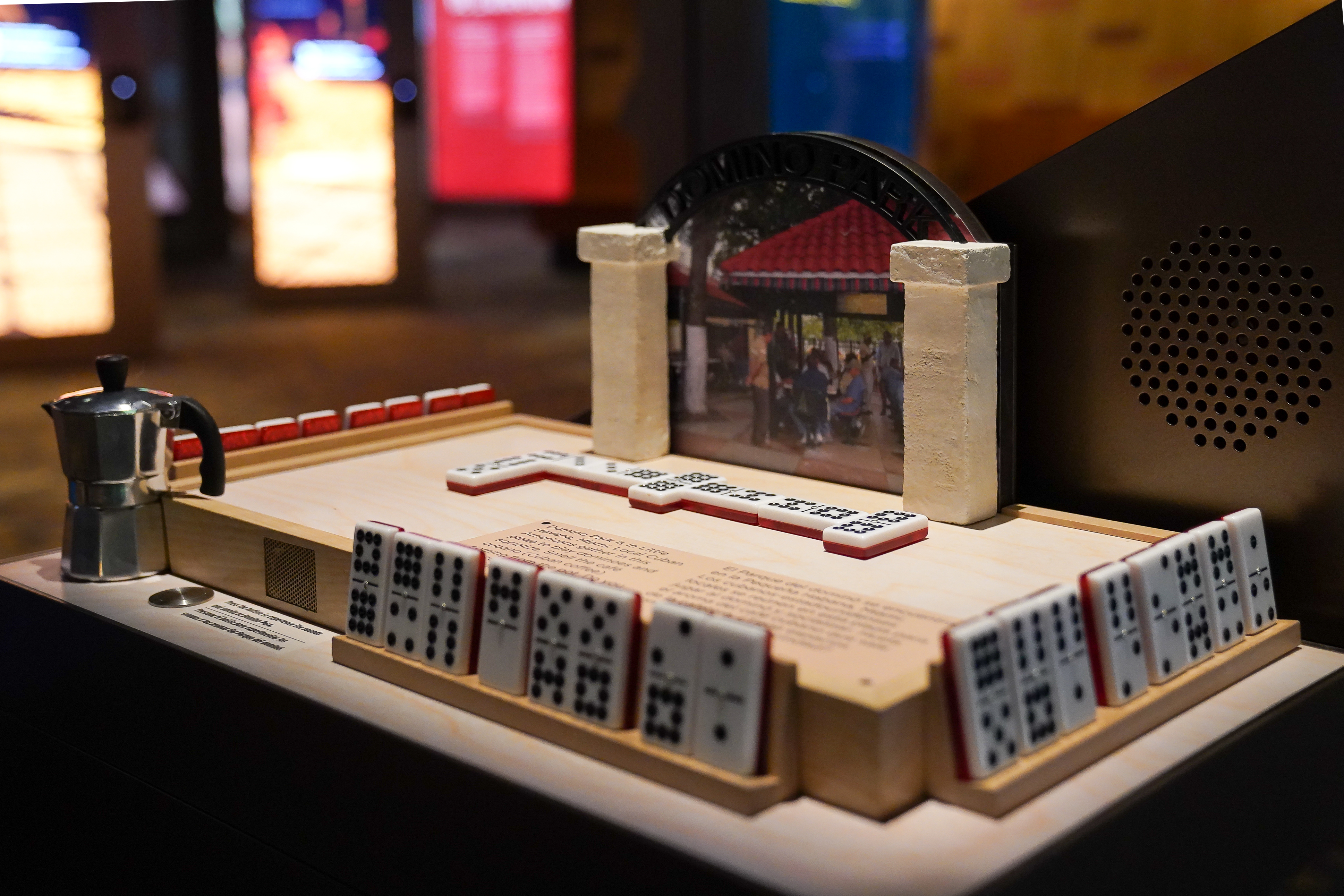 L2-0000082-D1-2022.08.02 Color photograph of the Domino Park touchable table with dominos arranged on a board and a miniature coffee pot.