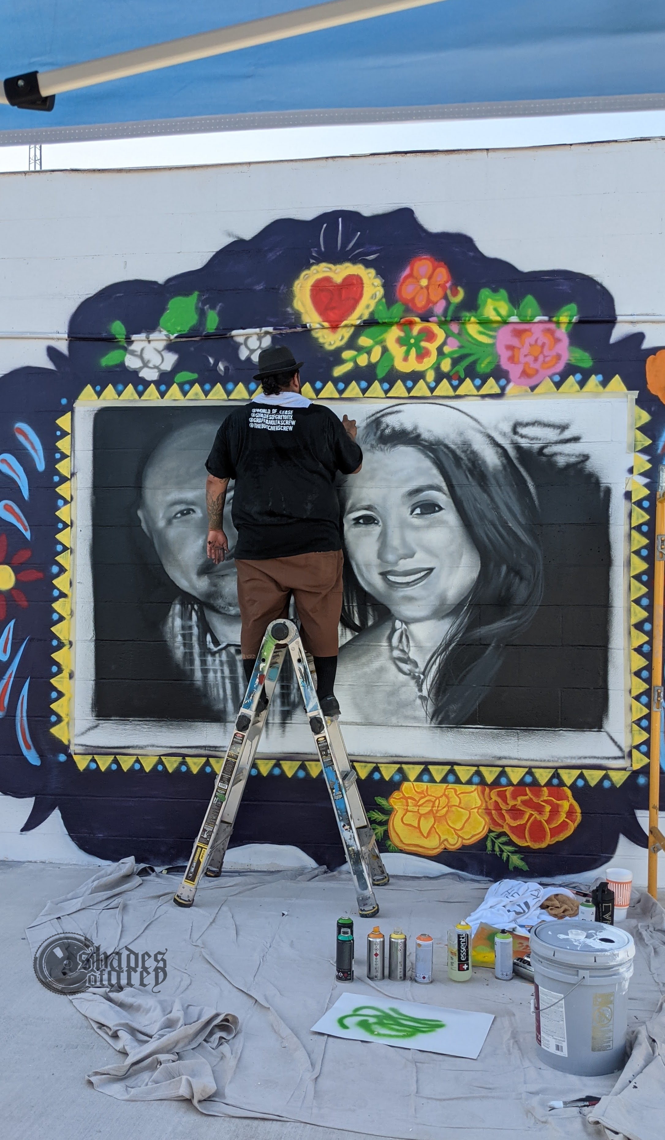 L2-0001153-D1-2022.10.10 Color photo of Cease Martinez on a ladder painting portrait mural for Irma and Joe Garcia.
