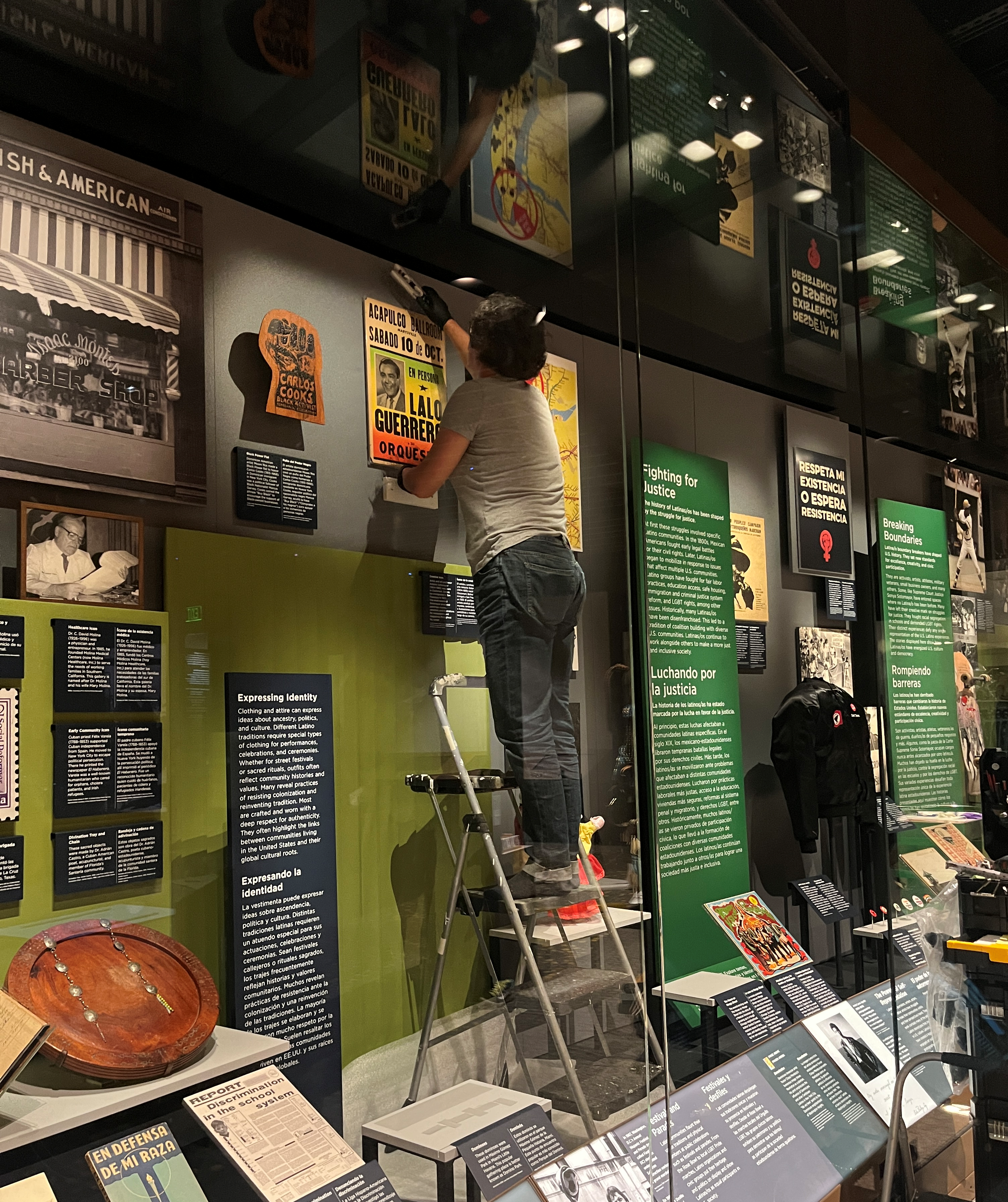 L2-0002205-D1-2023.05.22 Mount maker installing a poster in the exhibit case using a ladder