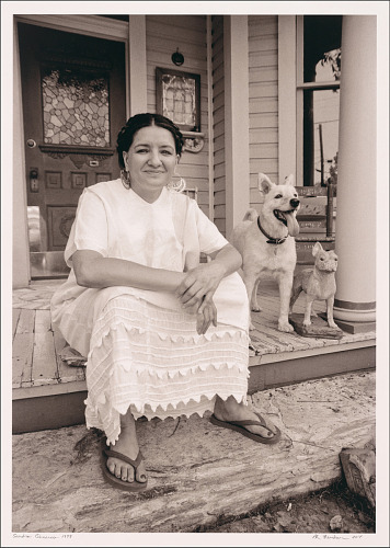 Sandra Cisneros and pet dog.jpg A woman (Sandra Cisneros) is sitting down at the front porch of a house with a dog next to her. She is wearing a traditional Mexican folk dress.
