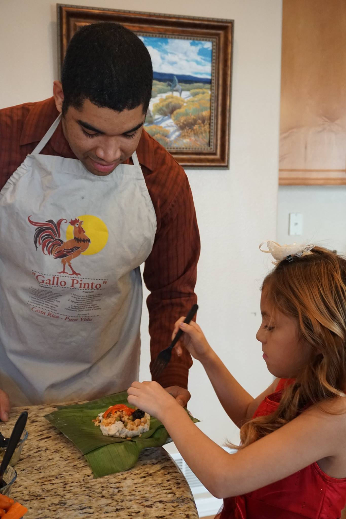 A man and a child are assembling a tamal on a plantain leaf.