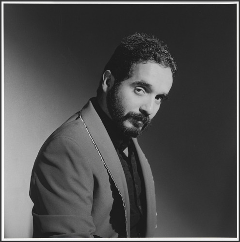 Willie Colon Portraiit of young Willie Colón standing sideways and looking at the camera. He is wearing a collar shirt and a blazer.